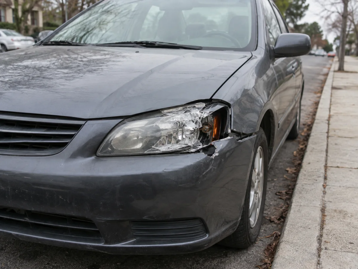 Front of a sedan with a cracked headlight lens and a missing piece of the housing