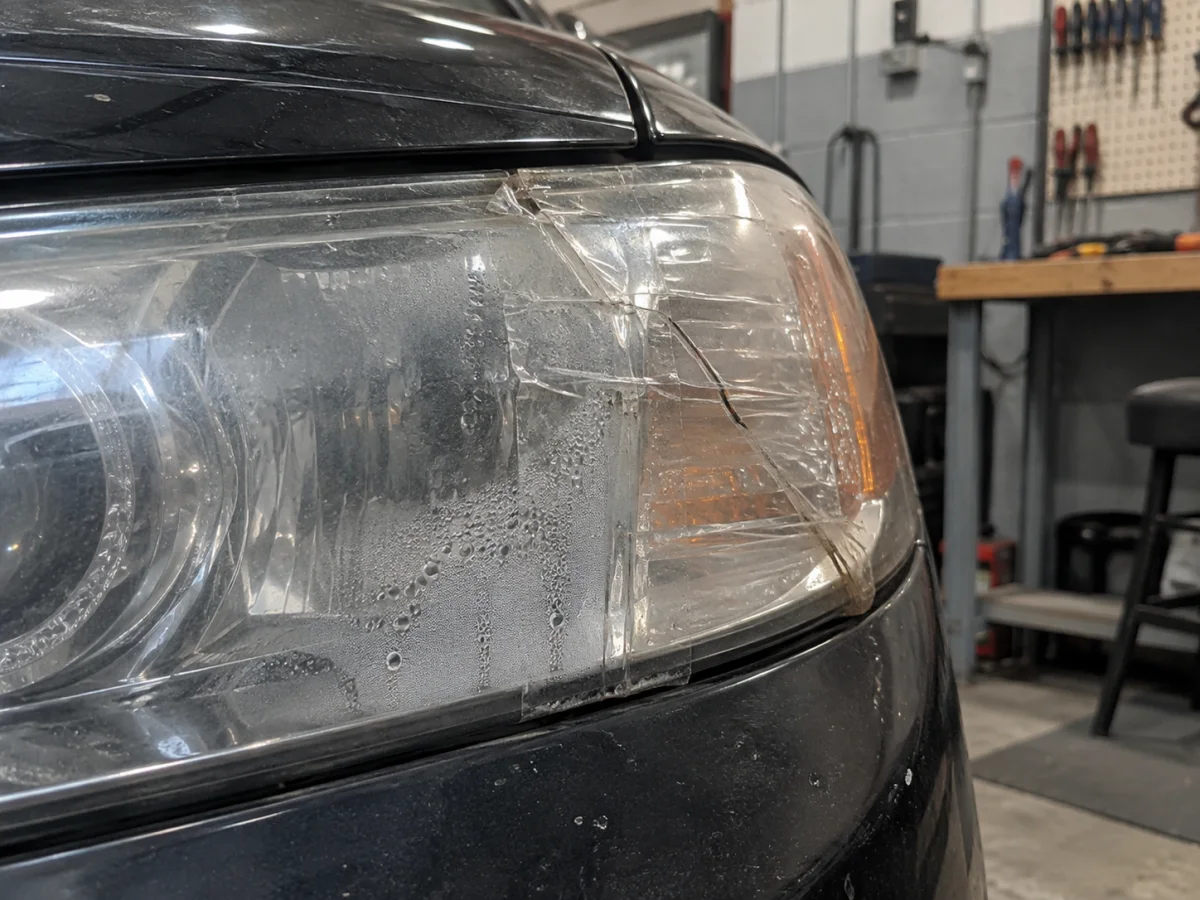 Headlight cover patched with clear tape over a crack, with fog forming inside