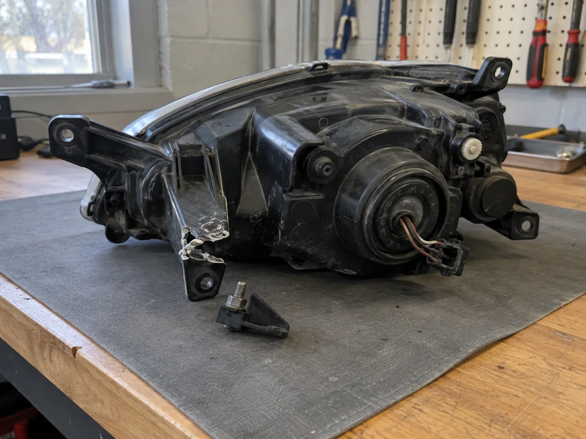 Back of a headlight housing with one plastic mounting tab snapped off at the base
