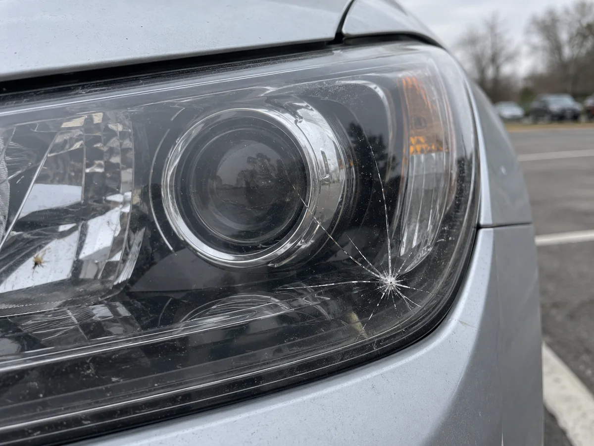 Cracked headlight lens with spider cracks spreading from a rock chip