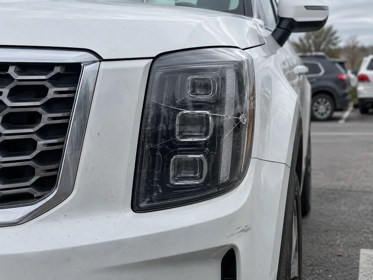 Front corner of a large Kia SUV with a crack running across the clear headlight lens