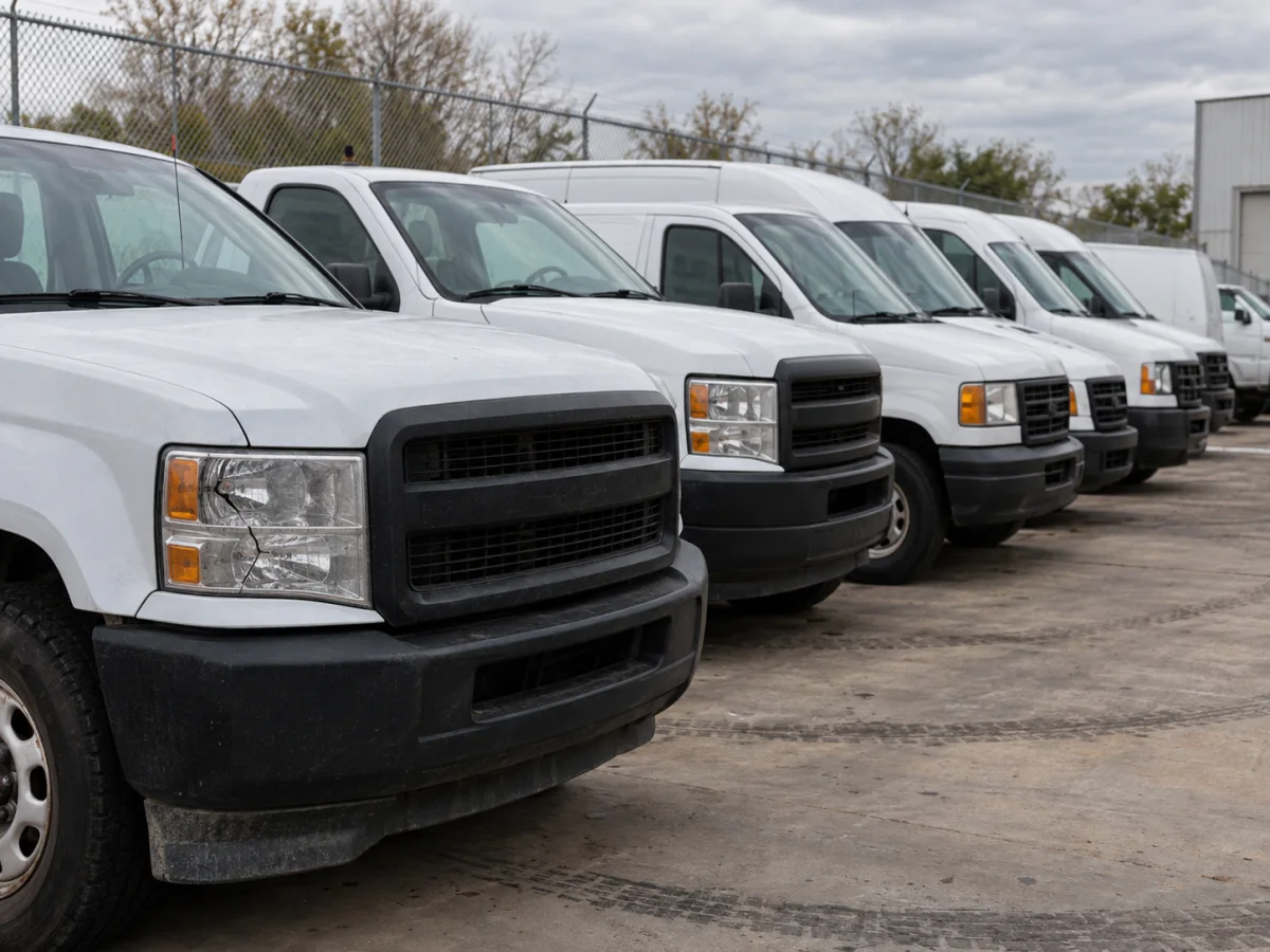 Row of fleet vans and pickup trucks parked at a depot, seen from the front with their headlights