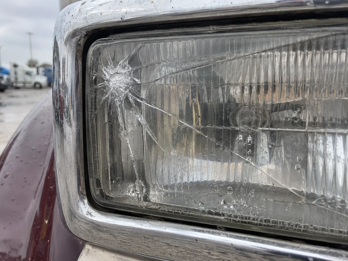 Close-up of a cracked outer lens on the headlight of a long-hood truck, with water marks behind it